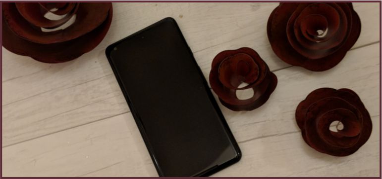 Google Pixel 2 XL laying on white wood and there are metal red roses around it.