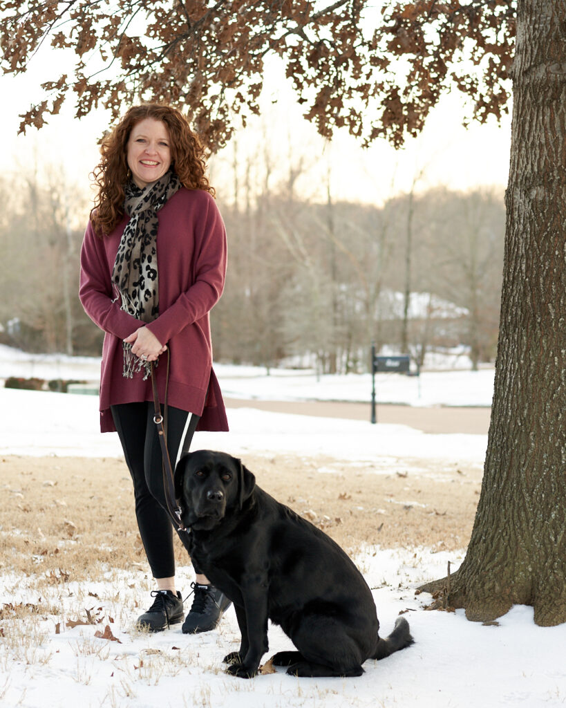 Jamie with Robin standing under a tree with Athleta wool/cashmere berry sweater and Athleta Metro 7/8 tights with white stripe down the side and Nike All Out Running shoes