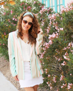 Close up shot of Jamie in spring colored blazer, cream camisole, Zara denim skirt in white and sunglasses ,earrings and headband . She is playing with her hair