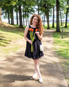 Life styled photo of dress with white sandals, white bag and white earrings. I am holding a bouquet of tulips.