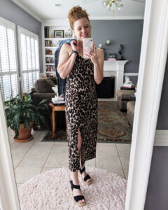 Life-styled version of dress with black espadrille wedges, holding a denim jacket and nickel and suede black earrings.