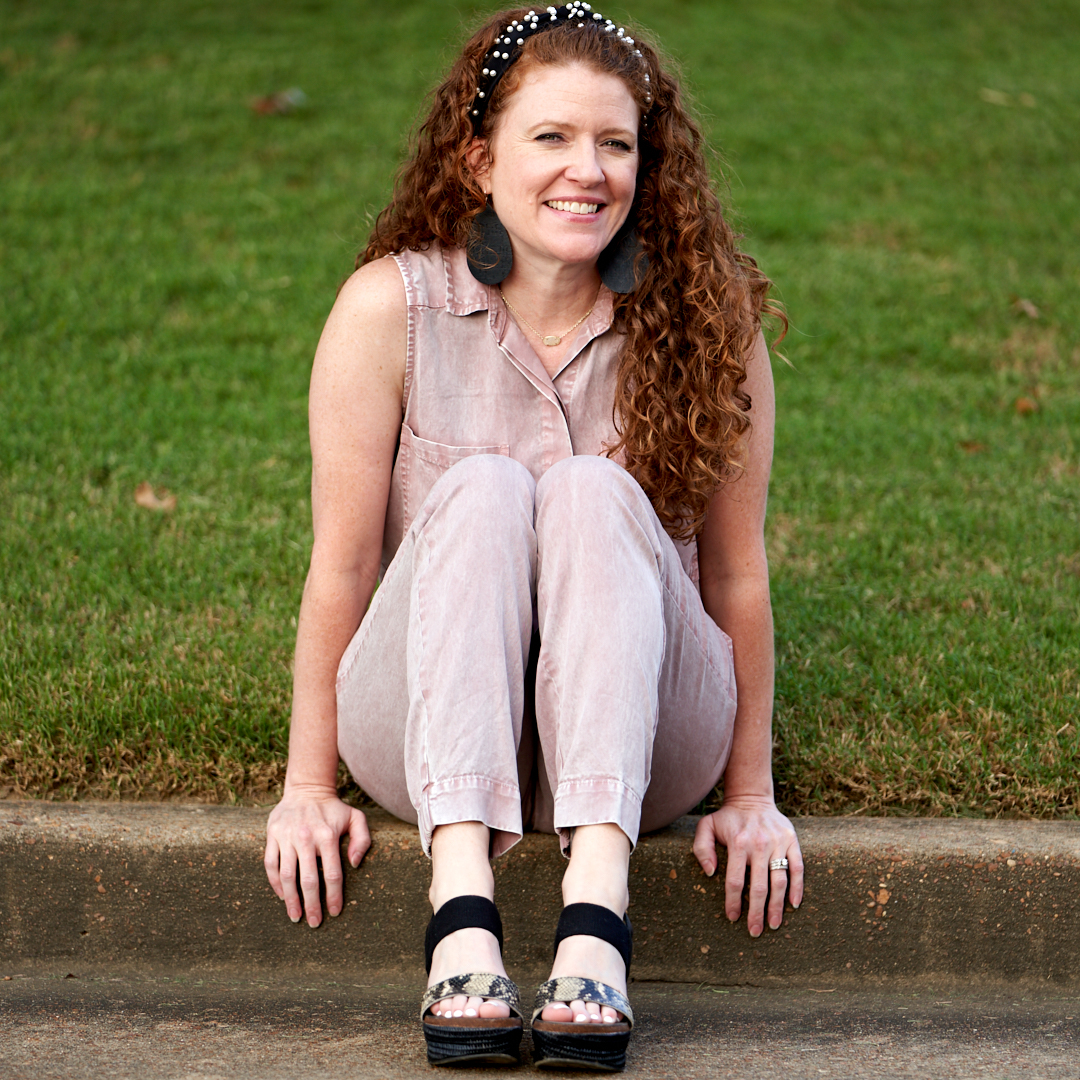 Jamie sitting on the curb by the grass wearing pink jumpsuit and OTBT Bushnell Wedges